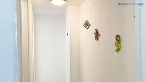 Un couloir aux murs blancs et doté d’un éclairage au plafond. Trois objets décoratifs sont accrochés au mur : un poisson bleu et blanc, un poisson rouge et bleu, et un poisson vert et jaune.