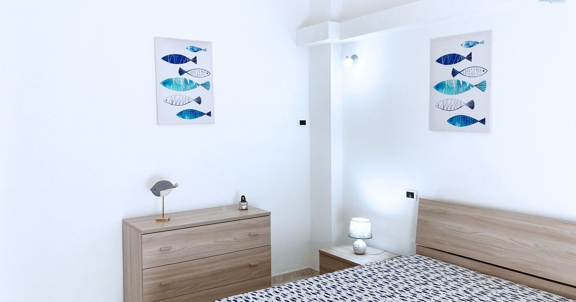 Ein Schlafzimmer mit einem Bett, einem Nachttisch, einer Kommode und zwei an der Wand befestigten Kunstwerken zum Thema Fische.