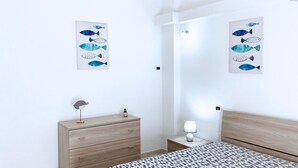Une chambre à coucher comprenant un lit, une table de chevet, une commode et deux œuvres d’art sur le thème des poissons, accrochées au mur.