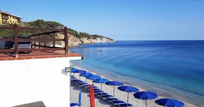 Una spiaggia con acqua cristallina, un pontile in legno con posti a sedere e ombrelloni.
