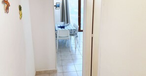 A narrow hallway leading to a dining area with a table and chairs, a window with curtains, and a door. - Casa Gioia - Le Ghiaie (Portoferraio)