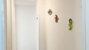 Un couloir aux murs blancs et doté d’un éclairage au plafond. Trois objets décoratifs sont accrochés au mur : un poisson bleu et blanc, un poisson rouge et bleu, et un poisson vert et jaune.