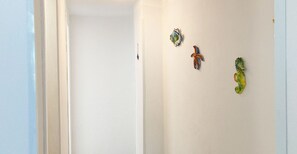 A hallway with white walls and a ceiling light. There are three decorative items on the wall: a blue and white fish, a red and blue fish, and a green and yellow fish. - Casa Gioia - Le Ghiaie (Portoferraio)