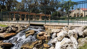 Un pont de pierre enjambant une cascade, avec une zone délimitée par une clôture et un belvédère en arrière-plan.