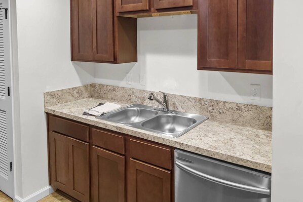 A kitchen with two sinks, wooden cabinets, and a stainless steel dishwasher.