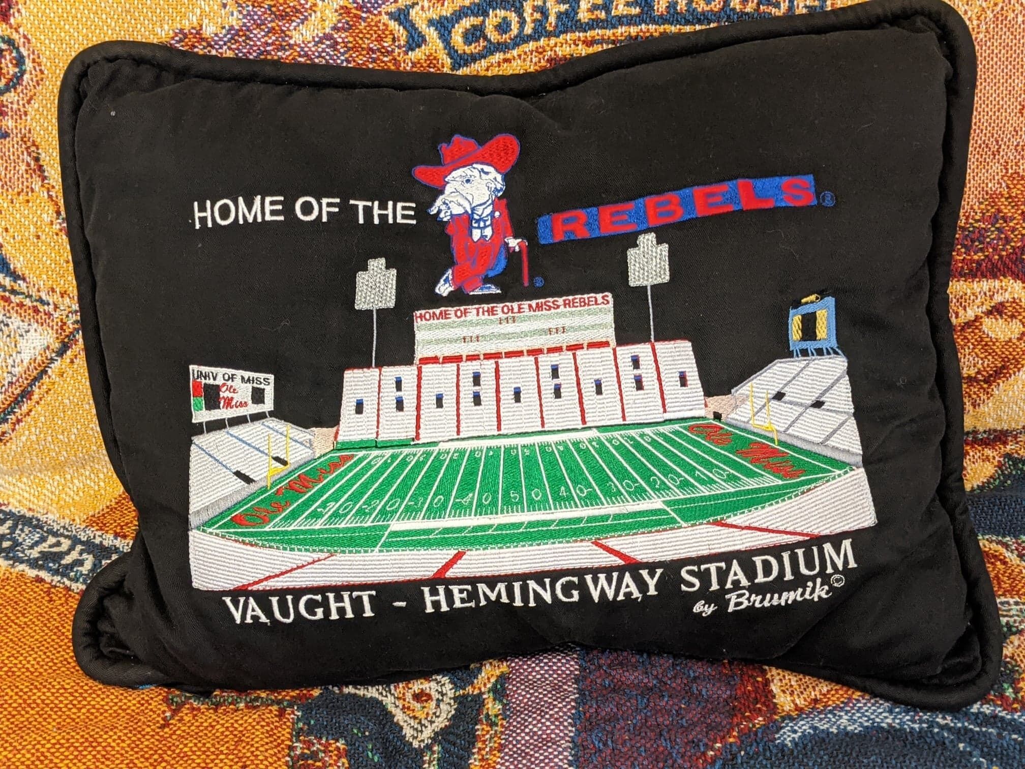Ein Kissen mit einem Design eines Football-Stadions, inklusive Maskotte sowie dem Text "HOME OF THE OLE MISS REBELS" und "VAUGHT - HEMINGWAY STADIUM".