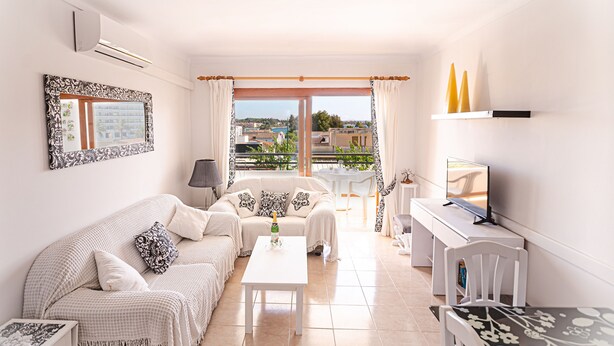 A living room with a sofa, coffee table, and TV, with a balcony and city view. - 2 bedroom apartment 200 m. from the beach (Alcúdia)