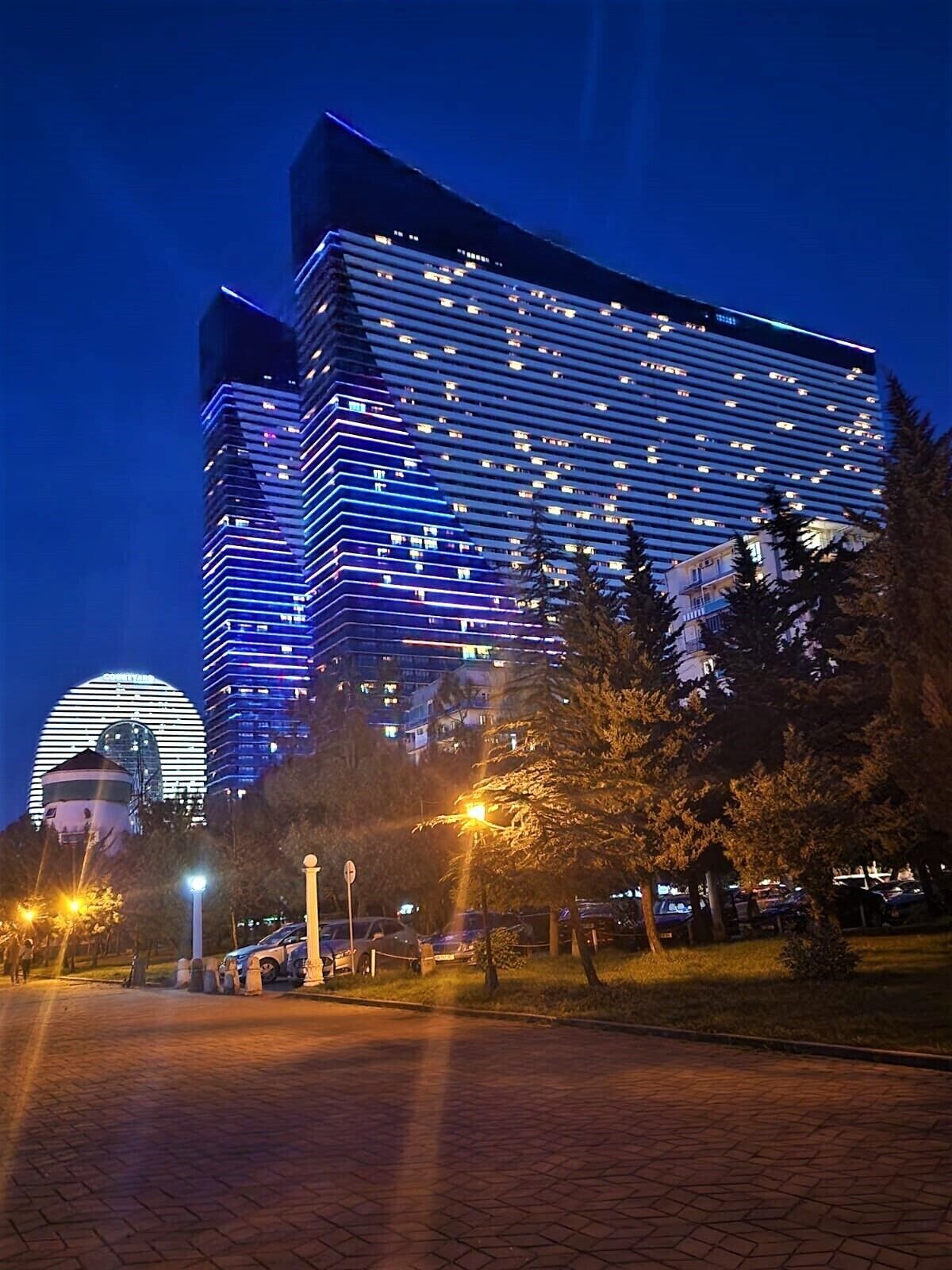 A modern hotel with a prominent glass facade, multiple floors, and a dome structure in the background.