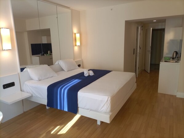 Una habitación de hotel moderna con una cama grande, una mesita de noche, un espejo y un baño visible a través de una puerta abierta.