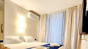 A hotel room with a bed, a flat-screen TV, an air conditioning unit, and a window with curtains. - Orbi City Apartment (Batumi)