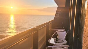A balcony with a view of the sunset over the water, a table with a bottle, and two wicker chairs. - Orbi City Apartment (Batumi)