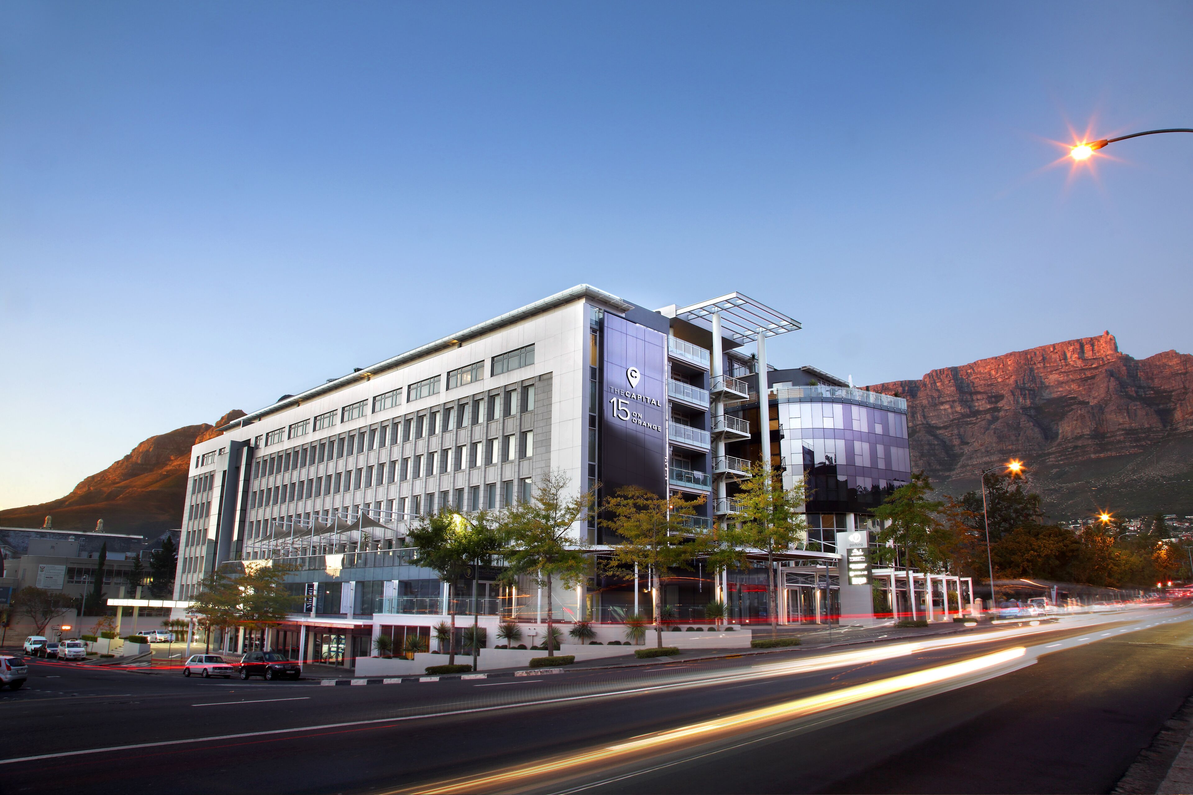 A modern hotel with a prominent '15' sign, indicating 15th floor, set against a mountainous backdrop.