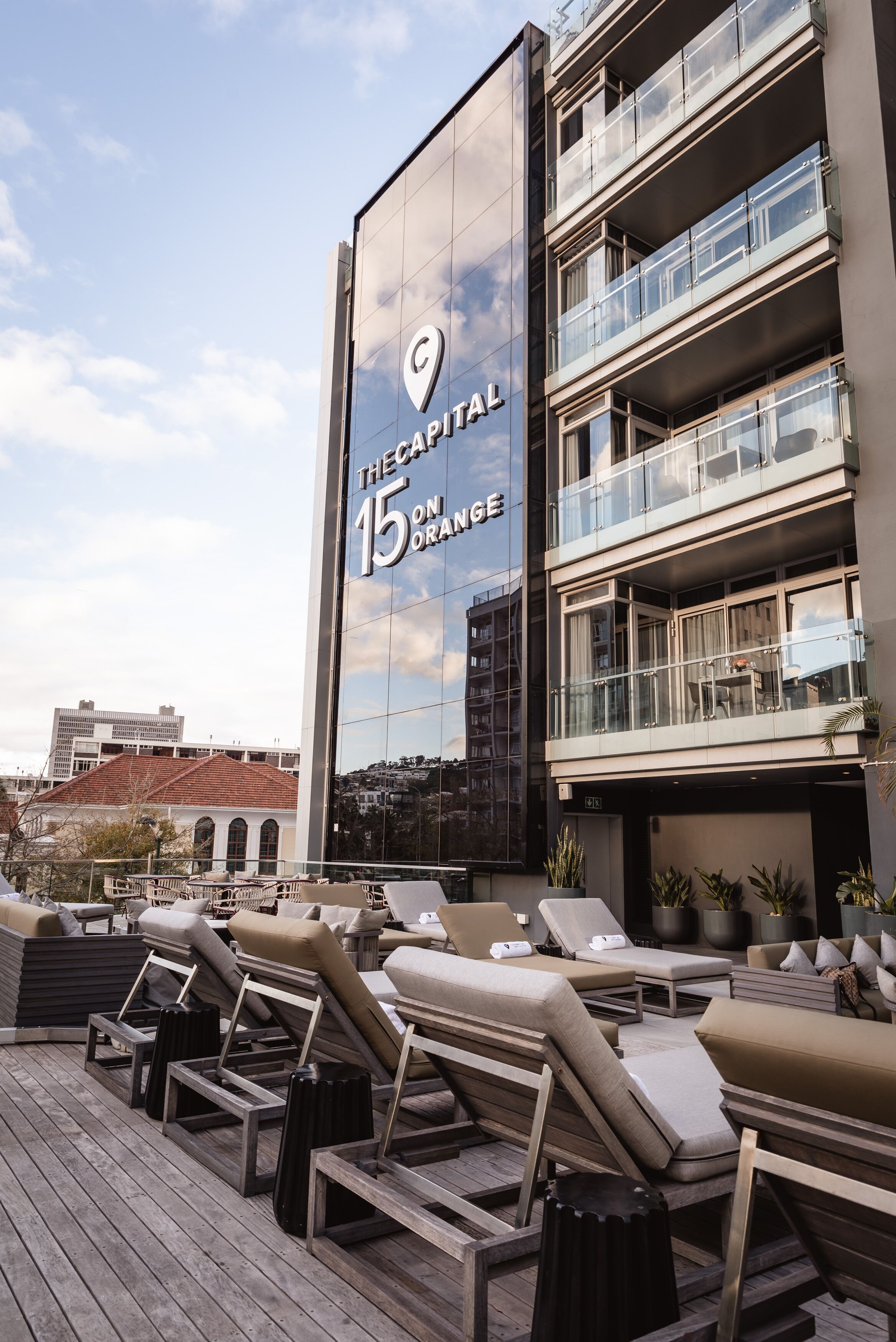 A rooftop lounge area with sun loungers and a view of a building with a glass facade and balconies.