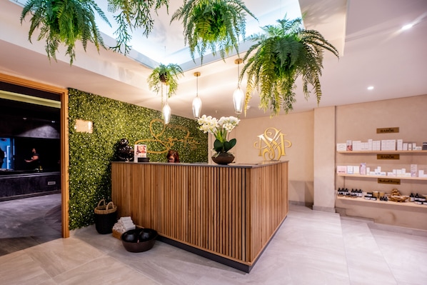 A reception area with a wooden reception desk, green foliage, and a sign that reads "Bazar."