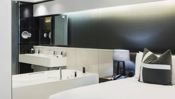 A modern hotel room with a large bed, a built-in vanity with a mirror, and a bedside table with a lamp.