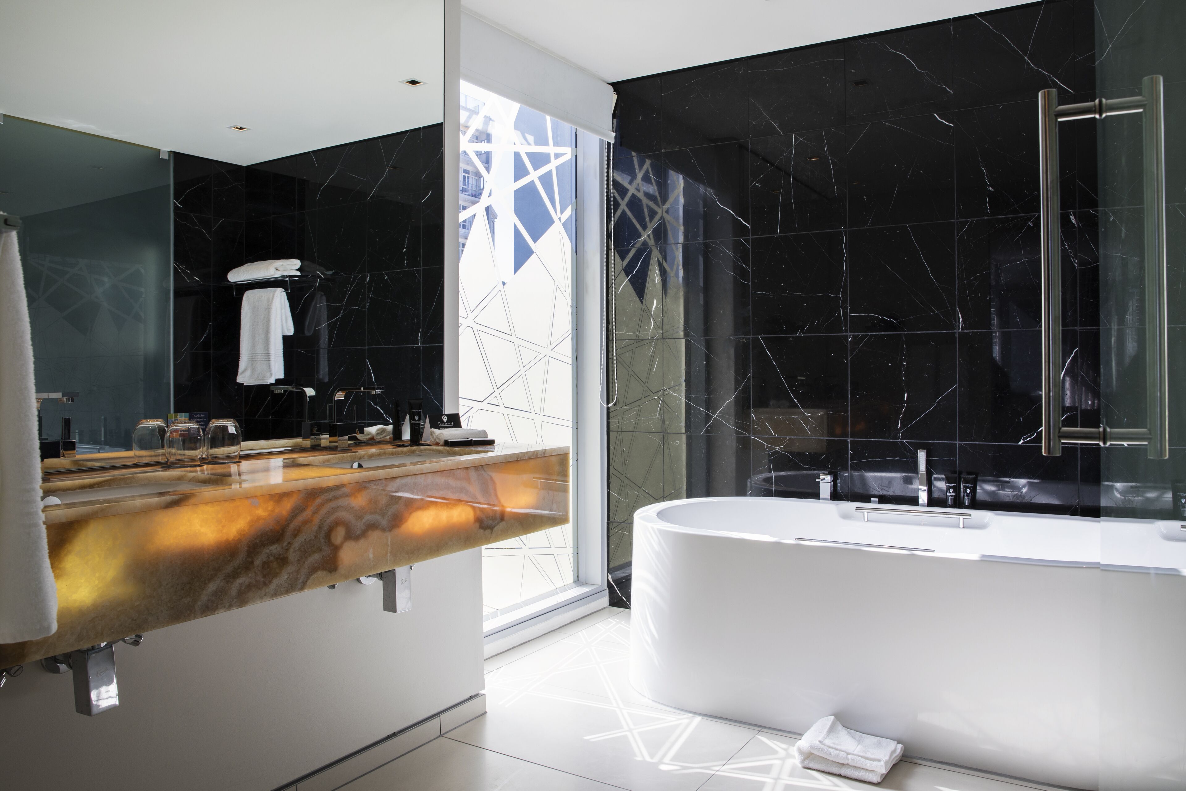 Un baño moderno con tocador de mármol, una bañera grande y un box de ducha de cristal.