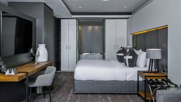 Una habitación de hotel moderna con cama, escritorio, silla, televisor, lámpara y armario.