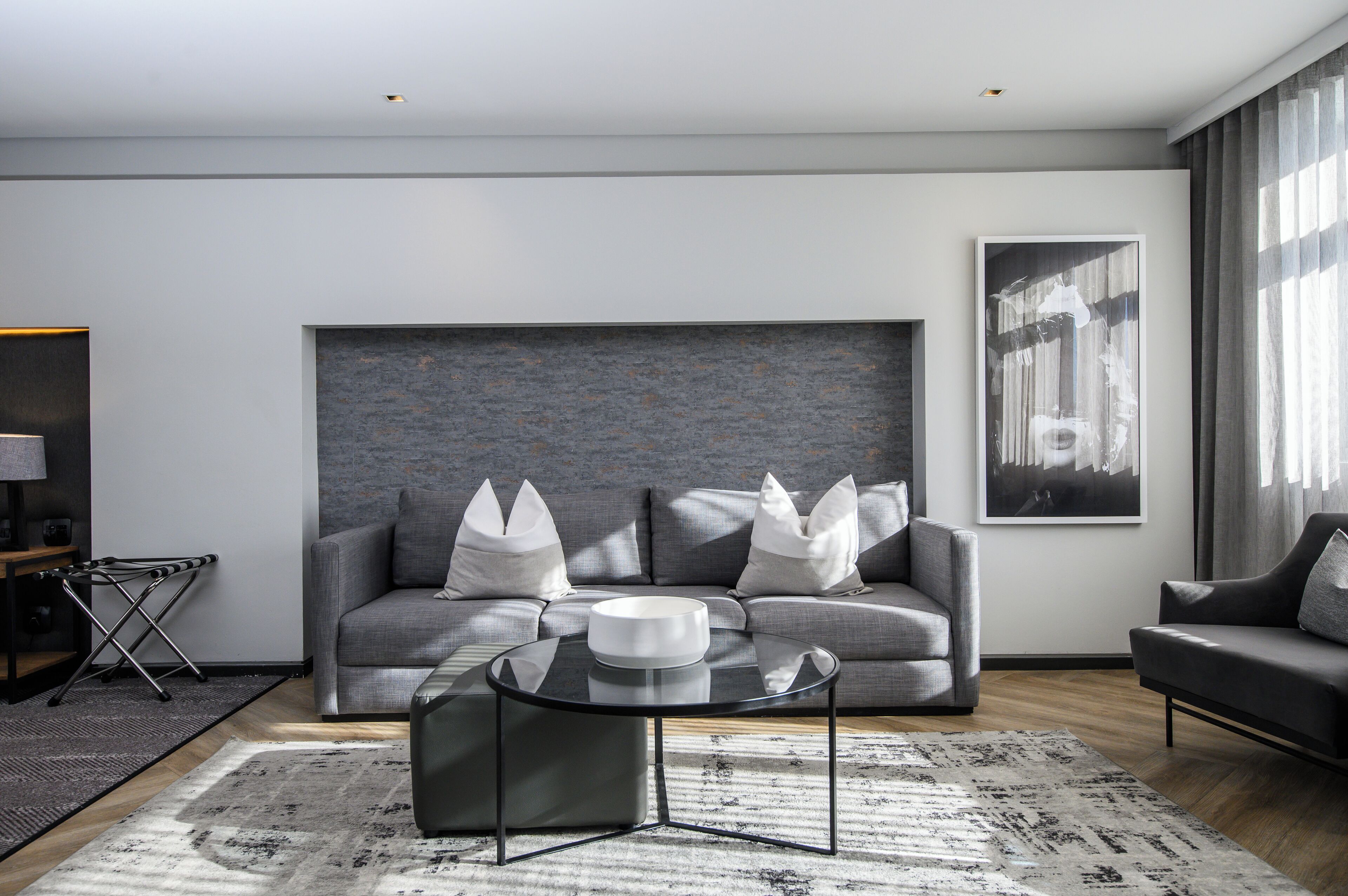 A modern living room with a grey sofa, a glass coffee table, and a large abstract painting on the wall.