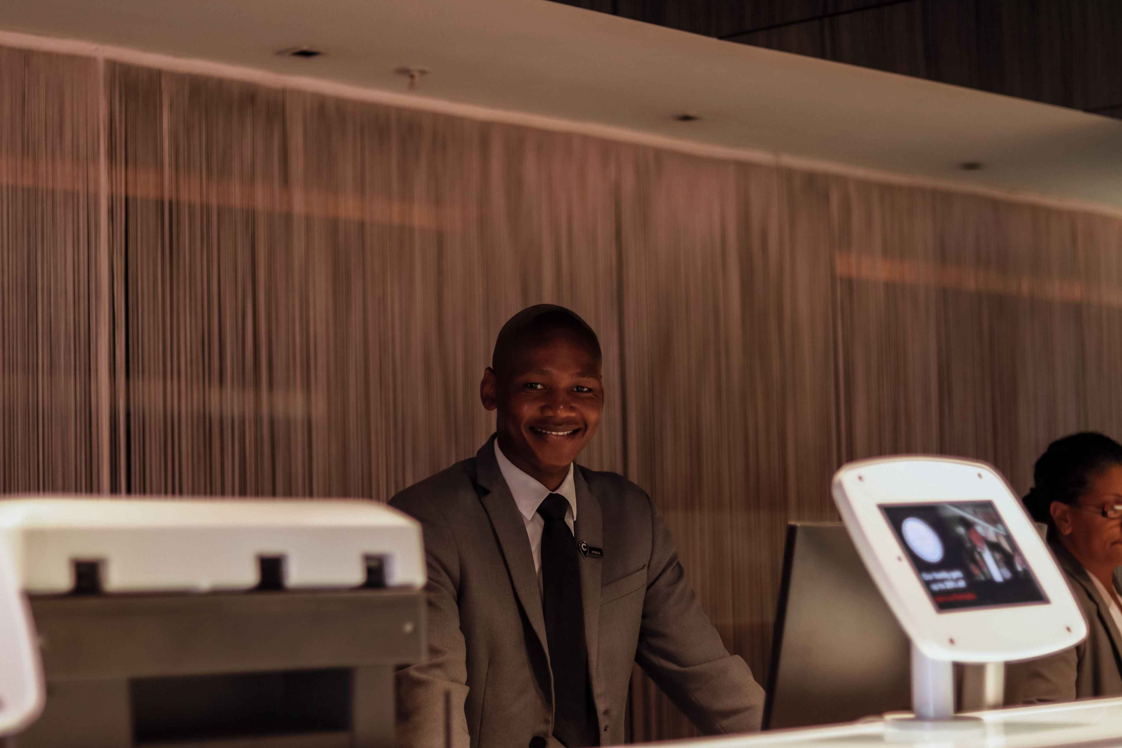 A man in a suit standing in front of a check-in kiosk with a digital display.