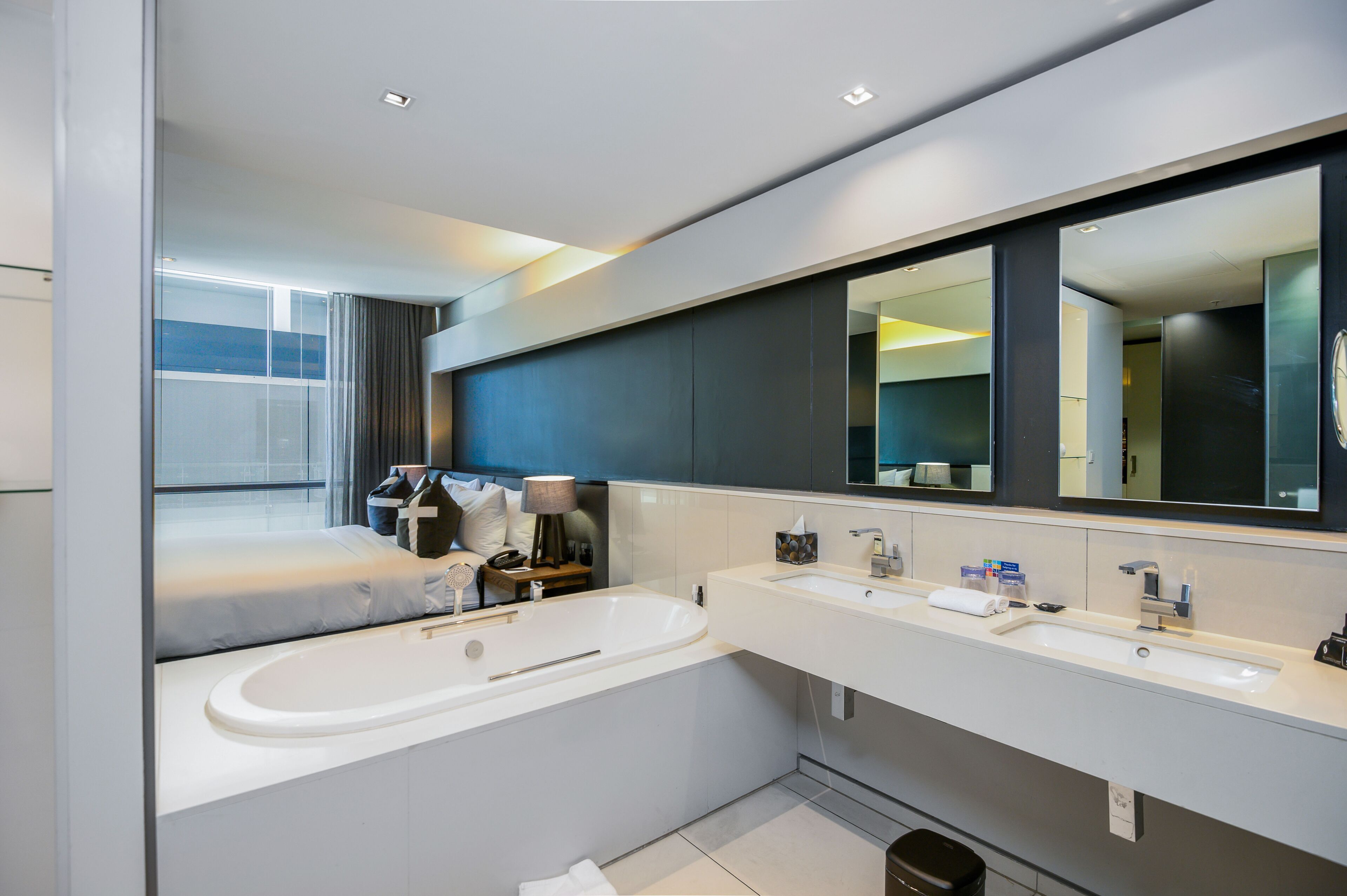 A modern hotel bathroom with a large bathtub, two sinks, and a large mirror.
