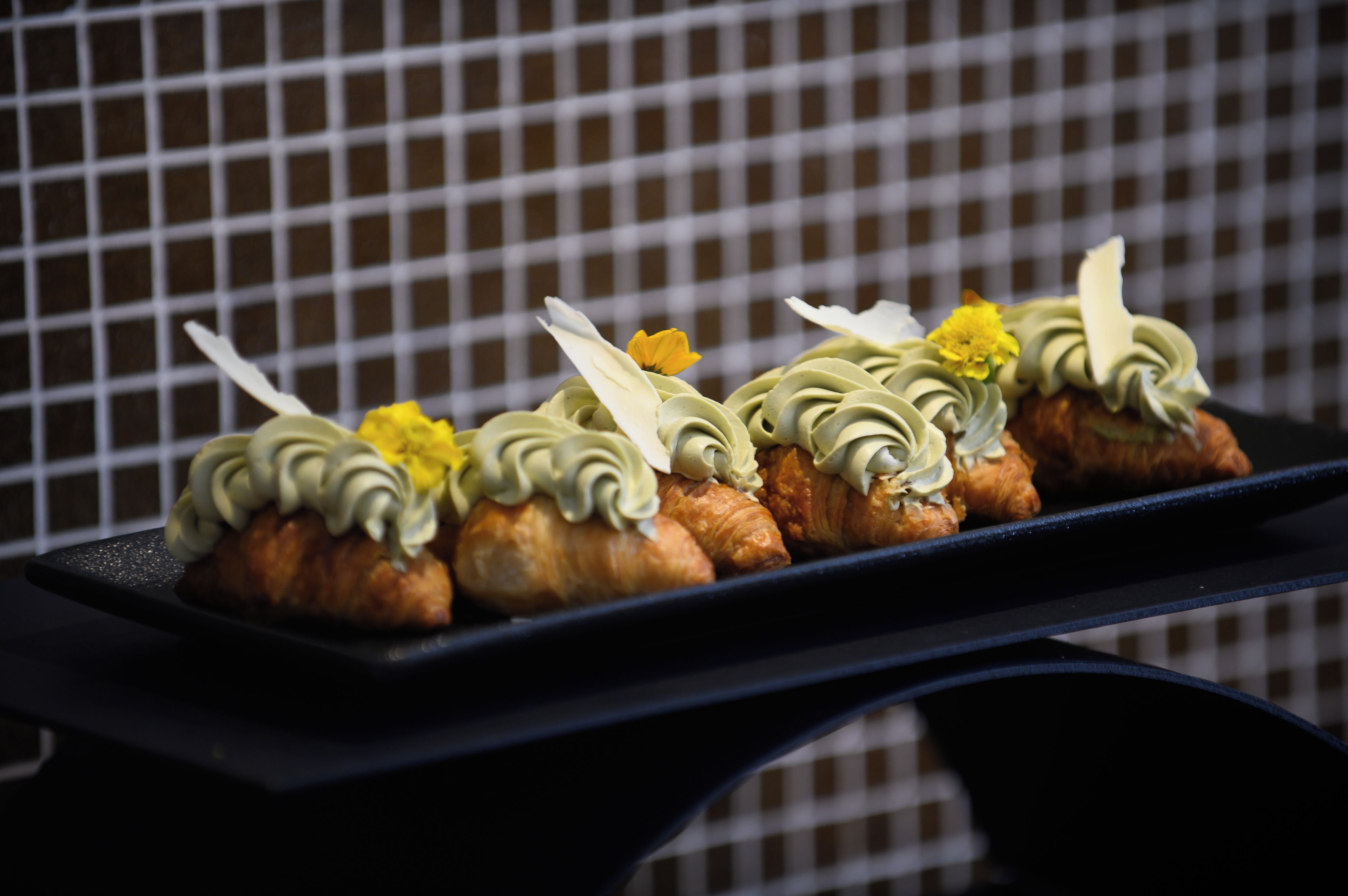A tray of pastries with cream and yellow flowers on a black plate.