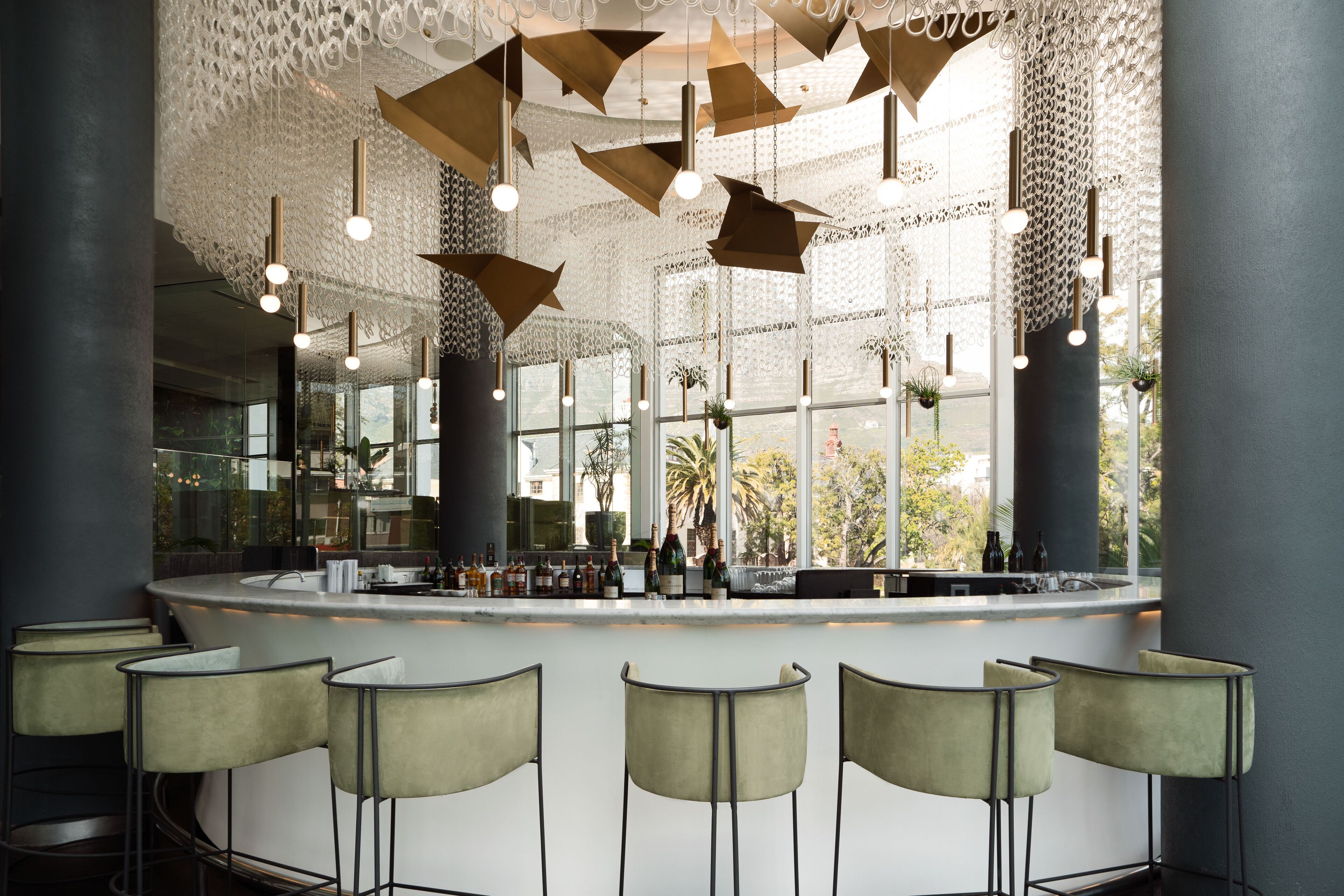 A modern bar area with a curved counter, multiple bar stools, and hanging pendant lights.