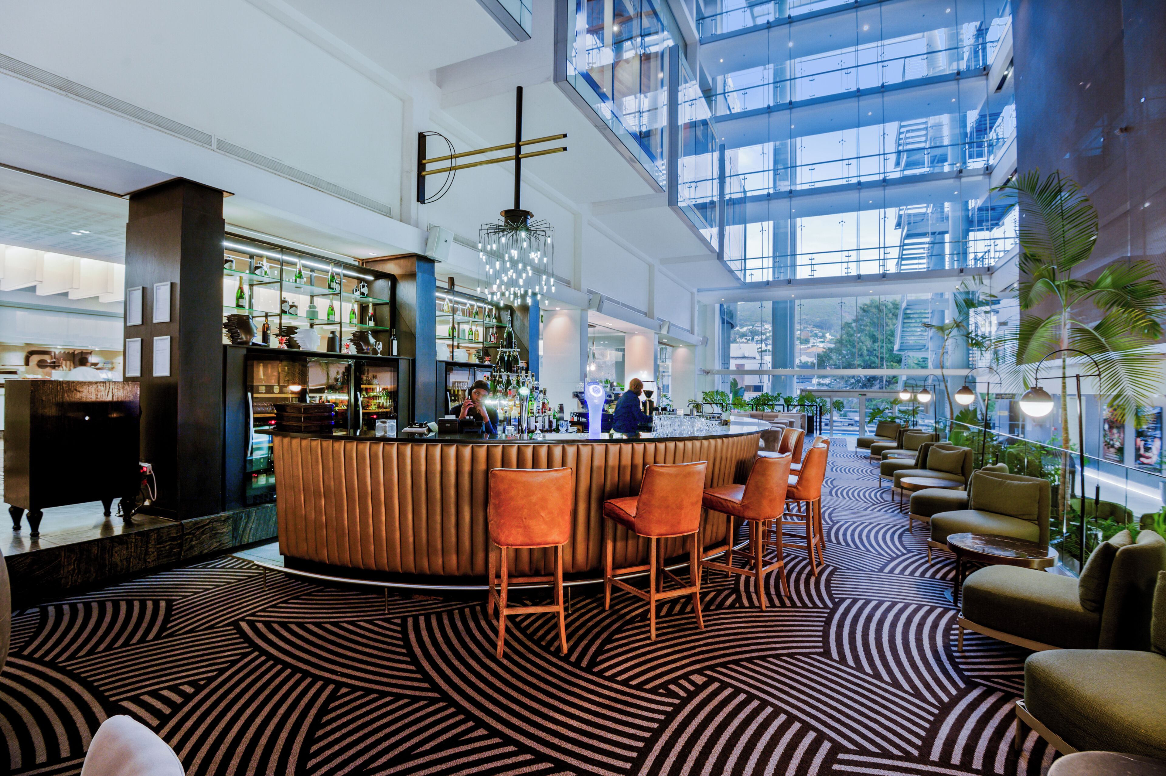A modern bar area with a high ceiling, large windows, and a patterned carpet.