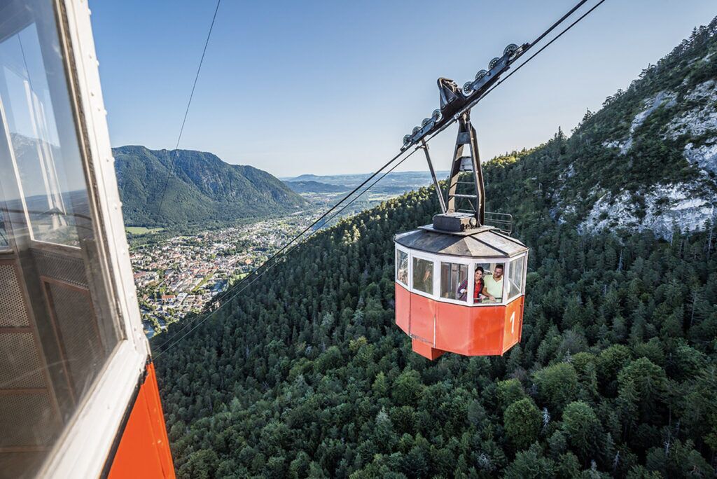 A cable car suspended over a forested mountain area.