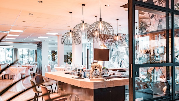 Zona de bar moderna con mostrador de madera, varias lámparas colgantes y una vitrina de cristal con diversos objetos.