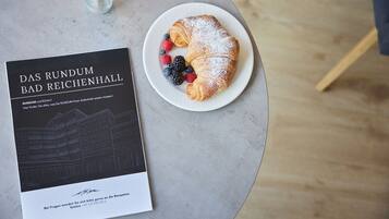 Un livre intitulé « Das Rundum Bad Reichenhall » est posé sur une table, à côté d’une assiette contenant des aliments, notamment une pâtisserie et des baies.
