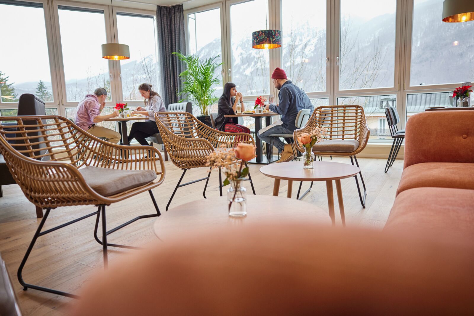 A cozy indoor seating area with wicker chairs and a round table, large windows with a view of mountains, and a warm ambiance.