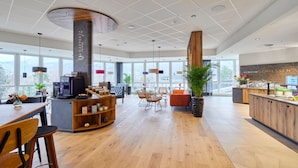 Una cafetería amplia con mostrador central, zona de mesas y ventanas grandes.