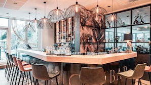 Zona de bar con mostrador de madera, varios taburetes y lámparas colgantes.