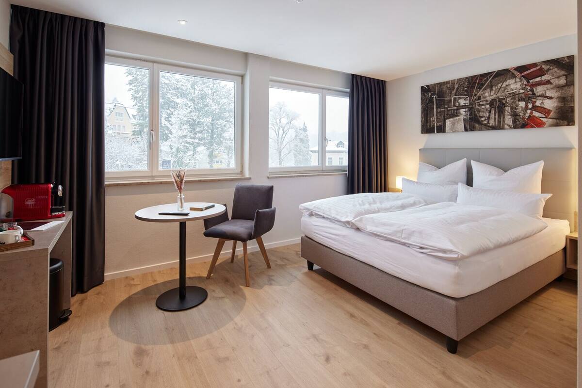 A hotel room with a bed, a desk, a chair, and a small table.