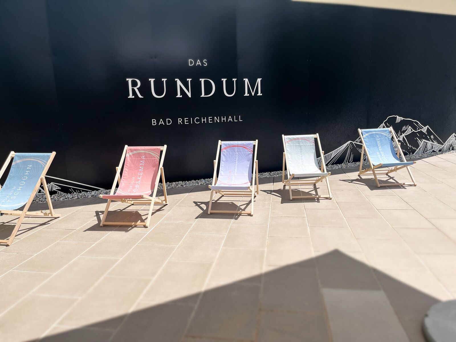Una fila de sillones de descanso frente a un muro con el texto 'DAS RUNDUM BAD REICHENHALT'.
