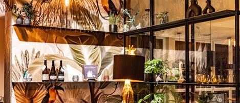 Un espace bar bien éclairé, avec des étagères remplies de bouteilles, une grande lampe et divers objets décoratifs.