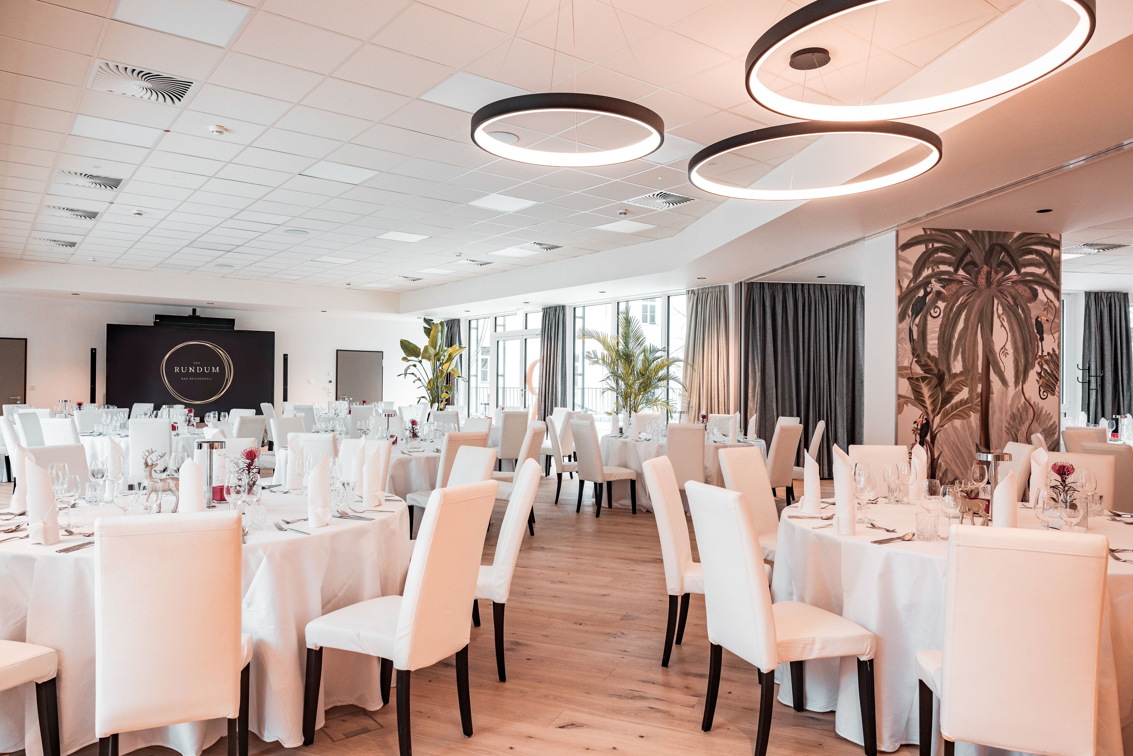 Un vaste espace dédié à la salle à manger, avec des tables rondes, des chaises blanches et des luminaires modernes.