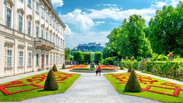Un jardín formal con parterres simétricos, un camino central y un edificio grande de arquitectura clásica.