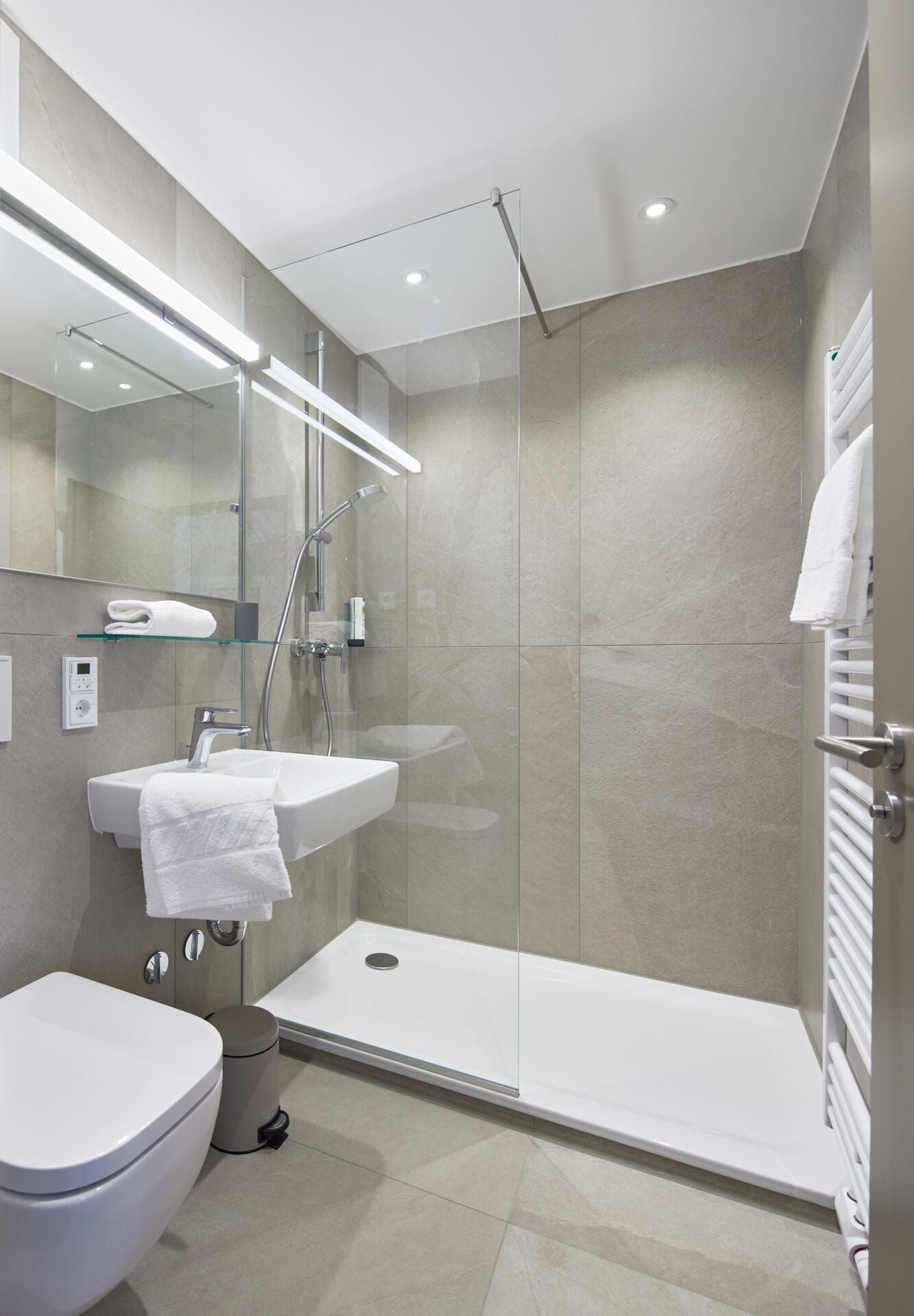 Een moderne badkamer met een douchecabine van glas, een witte wastafel en een toilet.