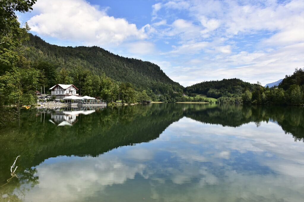 Un hotel junto al lago, con su reflejo en el agua, rodeado de colinas boscosas.