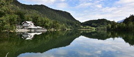 Un hotel junto al lago, con su reflejo en el agua, rodeado de colinas boscosas.
