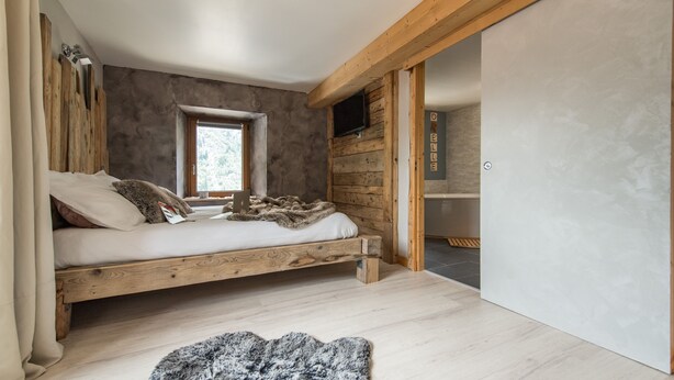 Un dormitorio con cama de madera, una ventana, alfombra de piel sintética y una pared de madera con un televisor.