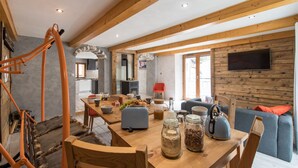 Un amplio espacio de sala con una mesa de comedor de madera, sillas y un sofá. Se aprecia una cocina al fondo con electrodomésticos modernos.