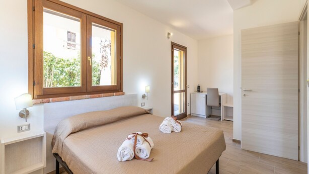 Ein Hotelzimmer mit Bett, Schreibtisch und Stuhl. Auf dem Bett liegen Handtücher und vom Fenster aus ist ein Blick auf Bäume möglich.