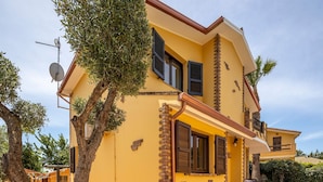 Ein gelbes Gebäude mit Balkon, Satellitenschüssel und kleiner Außenbestuhlung.