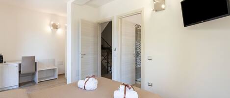 Habitación de hotel con cama, escritorio, silla, televisión y baño visible a través de una puerta abierta.