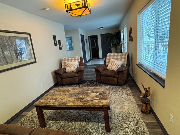 A living room with two brown armchairs, a checkered throw blanket, a patterned rug, and a wooden coffee table. - The Moose Is Inn -Large Group Retreat (Clam Gulch)