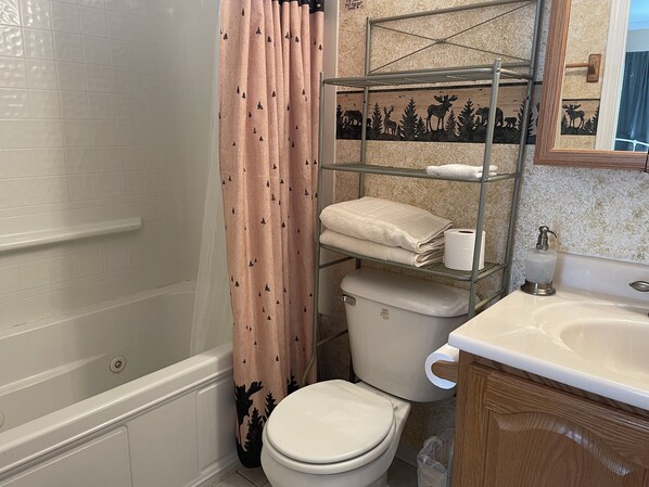 A bathroom with a toilet, a shower curtain, a shelf with towels, and a sink. - The Moose Is Inn -Large Group Retreat (Clam Gulch)