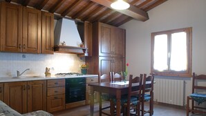 Une cuisine avec des meubles de rangement en bois, une table à manger avec des chaises et une fenêtre avec des stores.
