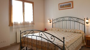 Une chambre à coucher avec un lit, une fenêtre ornée de rideaux en dentelle, un tableau accroché au mur et une table de chevet avec une lampe.